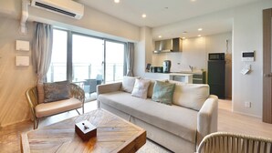 A modern living room with a sofa, a wooden coffee table, and a dining area with a kitchen in the background.