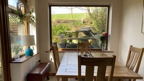 A dining area with a wooden table and chairs, a bench, and a window with a view of greenery.
