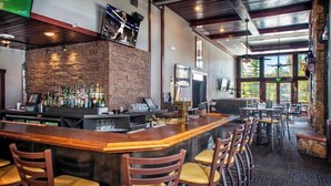 A bar area with a long counter, multiple stools, a brick wall, and a view of the outdoors through large windows. - Ski in, ski out resort at Grand Timber Lodge in beautiful Breckenridge, CO (Breckenridge)