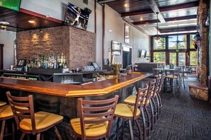 A bar area with a long counter, multiple stools, a brick wall, and a view of the outdoors through large windows. - Ski in, ski out resort at Grand Timber Lodge in beautiful Breckenridge, CO (Breckenridge)