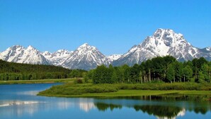 Un lac paisible dont les eaux reflètent une chaîne de montagnes, le tout étant entouré d’une forêt dense.