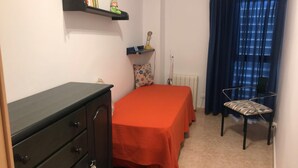 Ein kleines Schlafzimmer mit einem Bett, einem Sessel, einer Kommode, einer Heizung und einem Regal mit Büchern und einem Spielzeug.