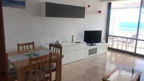 Ein modernes Wohnzimmer mit Essbereich, einem Flachbildfernseher und einem Balkon mit Meerblick.