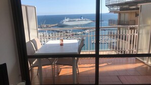 Ein Balkon mit Tisch und Stühlen mit Blick auf einen Yachthafen, wo Boote und ein Kreuzfahrtschiff liegen.