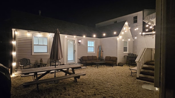 Un espace extérieur abrité, équipé d’une table de pique-nique, de bancs et de guirlandes lumineuses.
