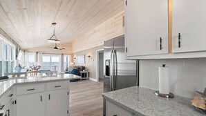 A modern kitchen with white cabinetry, a stainless steel refrigerator, and a marble countertop. - Salty Kisses & Starfish Wishes by Brunswick VR: Oceanfront & Pet-Friendly (Ocean Isle Beach)