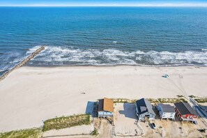 An aerial view of a beachside property with a sandy beach, a rocky breakwater, and several buildings with distinct architectural styles. - Salty Kisses & Starfish Wishes by Brunswick VR: Oceanfront & Pet-Friendly (Ocean Isle Beach)