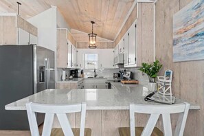 A modern kitchen with a central island, white cabinetry, and a wooden ceiling. - Salty Kisses & Starfish Wishes by Brunswick VR: Oceanfront & Pet-Friendly (Ocean Isle Beach)
