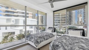 Un dormitorio moderno con ventanas amplias, un ventilador de techo y una cama con colcha estampada con hojas.