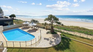 Zona de piscina con sillones de descanso y sombrillas, con vistas a una playa y al océano.