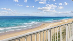Vista a la playa desde un balcón con barandilla, océano y costa lejana.