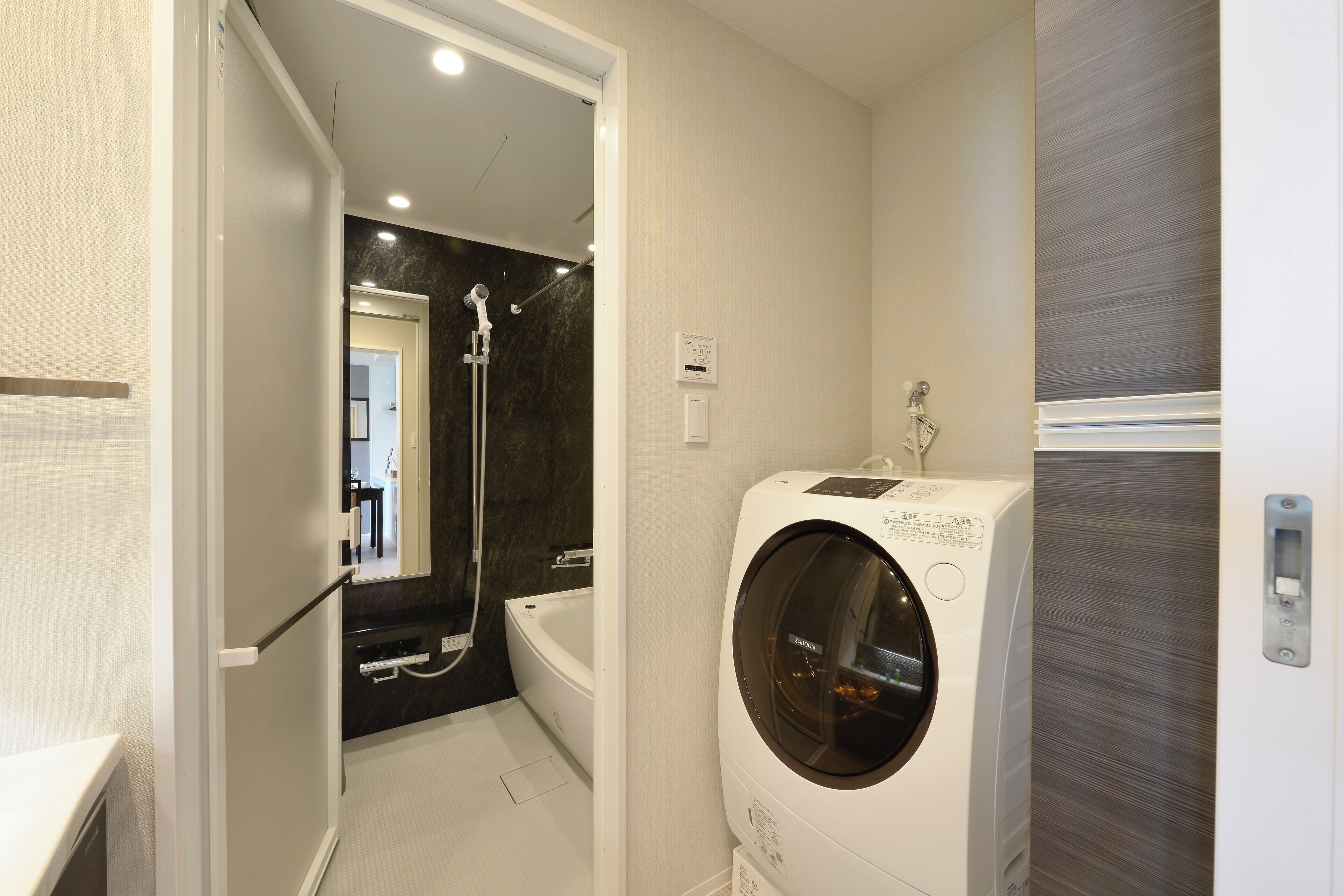 A compact bathroom with a built-in washing machine, a bathtub, and a shower.