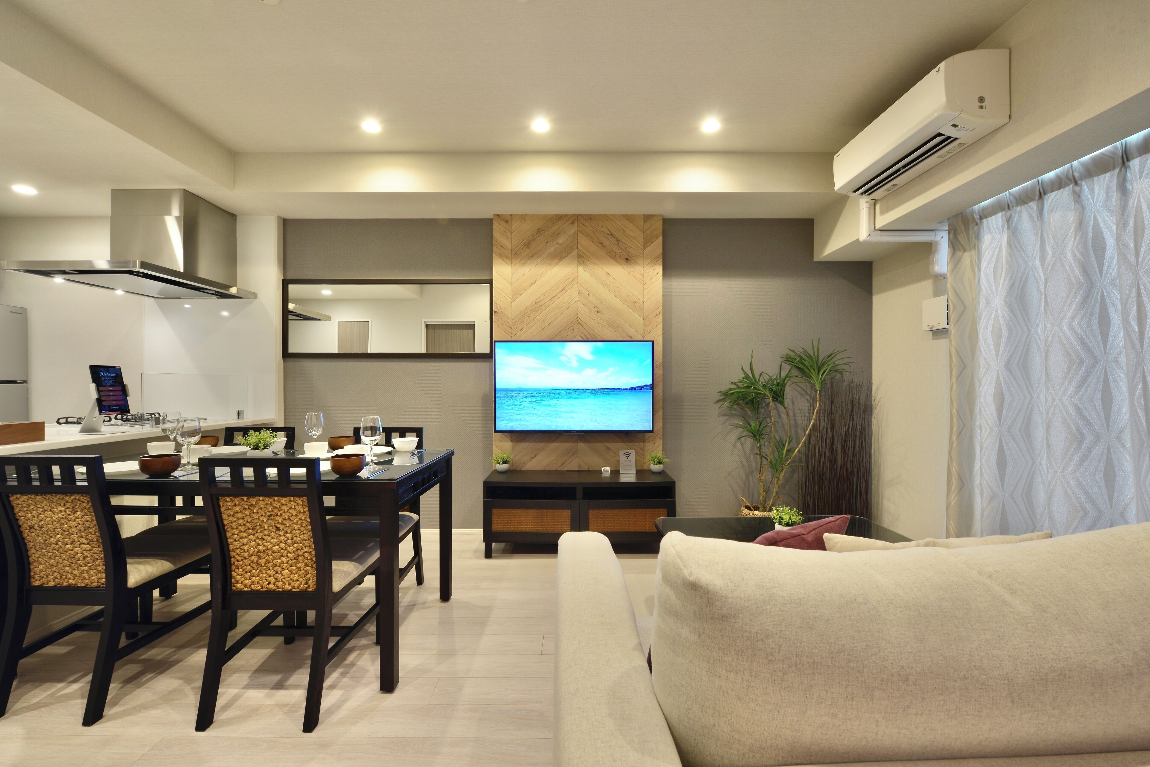 A modern living room with a large flat-screen TV, a dining area with wooden chairs, a sofa, and a potted plant.
