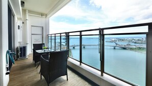 A balcony with a view of a body of water and a bridge, furnished with wicker chairs and a table. - Branchera naha akebono premist R69 (Naha)