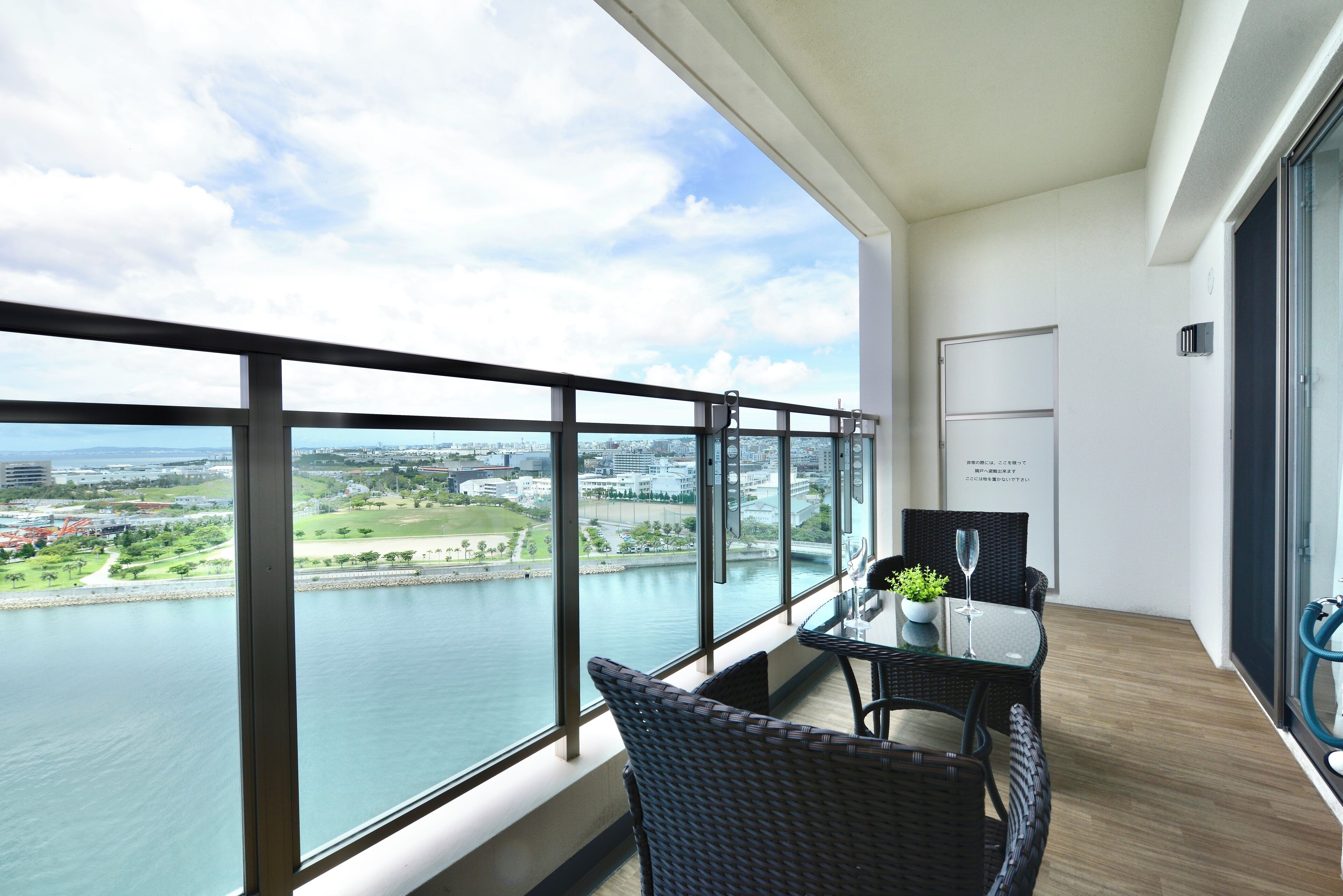 A balcony with a view of a river and cityscape, furnished with wicker chairs and a table.