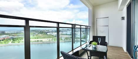 A balcony with a view of a river and cityscape, furnished with wicker chairs and a table.