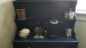 A dark blue cabinet with a honeycomb-patterned container, a coffee maker, a jar, and a bowl with a colorful design. - Adventure House: Fully Stocked Kitchen 5 mins from Michigan Tech (Hancock)
