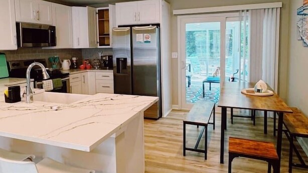 Une cuisine moderne avec des meubles blancs, un îlot central et un coin repas comprenant une table et des bancs en bois.
