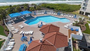 A rooftop pool with multiple sections, surrounded by lounge chairs and umbrellas, overlooking the ocean. - ☀️Beachfront☀️ 2Br 2Ba with Heated Pool, Playground, Gym, and Arcade! (North Topsail Beach)