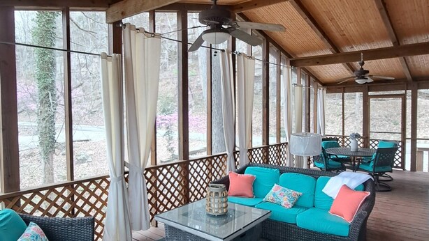 A covered outdoor seating area with wicker furniture and cushions, a glass-top coffee table, and a ceiling fan. - Serene Lakefront Cottage Home, relax and enjoy! Walk right to the water. (Westview)
