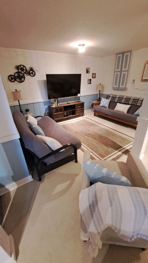 Una sala de estar con un sofá, una silla, un televisor y un mueble aparador.