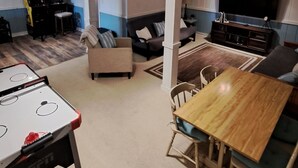 A living room with a sofa, a coffee table, a TV, and a foosball table. - Serene Lakefront Cottage Home, relax and enjoy! Walk right to the water. (Westview)