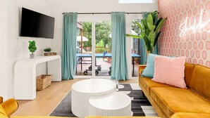 Een moderne woonkamer met een bank, een salontafel, een aan de muur bevestigde televisie en een schuifdeur die leidt naar een buitenruimte.
