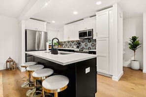 Una cocina moderna con armarios blancos, un refrigerador de acero inoxidable, un microondas y una isla negra con taburetes.