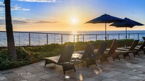 Une terrasse dotée de chaises longues et de parasols, offrant une vue sur la mer au coucher du soleil.