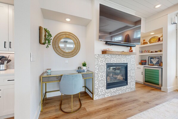 A modern kitchen with a built-in stove, a dining area with a glass table and a blue chair, and a TV mounted above the stove. - Resort Style Pools, Golf Cart Boardwalk to the Beach (Port Aransas)