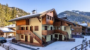 A multi-story wooden chalet with balconies, a staircase, and a snow-covered ground. - Condominio Parco degli abeti by Interhome (Canazei)