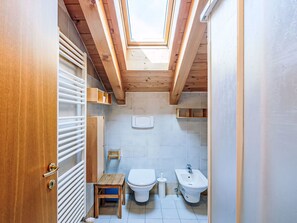 Une petite salle de bain avec un puits de lumière, des poutres en bois, des toilettes, un bidet et un petit tabouret en bois.
