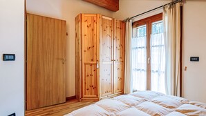 A bedroom with a wooden wardrobe, a bed with a white duvet, and a window with curtains. - Condominio Parco degli abeti by Interhome (Canazei)