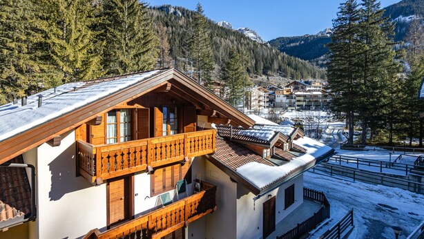 A chalet with a wooden balcony, snow-covered roof, and a view of a mountainous area. - Condominio Parco degli abeti by Interhome (Canazei)