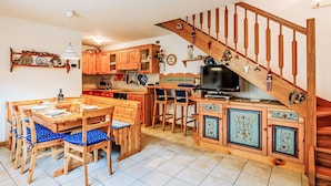 A cozy kitchen with wooden cabinets, a dining table with blue chairs, and a wooden staircase. - Condominio Parco degli abeti by Interhome (Canazei)