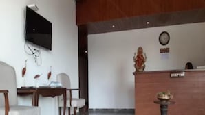 A reception area with a wooden desk, a reception counter, and a statue on the wall. - Shashwat Grand Valley (Dehradun)