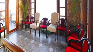 A room with stone walls, large windows, and a ceiling fan. There are several chairs with red cushions and a wooden table. - Shashwat Grand Valley (Dehradun)