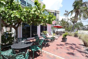 An outdoor seating area with green metal chairs and tables, a red umbrella, and potted plants. - Beach Tree across street from beach (Siesta Key)