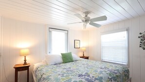 A bedroom with a bed, two bedside tables with lamps, a ceiling fan, and two windows with blinds. - Blue Dolphin Cottage steps from the beach (Siesta Key)