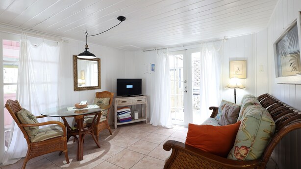 A living room with a dining table, wicker chairs, a sofa, and a television. - Blue Dolphin Cottage steps from the beach (Siesta Key)