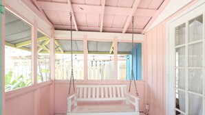 A pink-walled porch with a white swing bench, a wooden fence, and a blue door. - Blue Dolphin Cottage steps from the beach (Siesta Key)