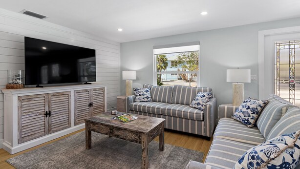 A living room with a large flat-screen TV, striped sofas, and a wooden coffee table.