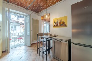 Une cuisine équipée d’un réfrigérateur en acier inoxydable, un coin repas avec une table et des chaises, un luminaire suspendu et un tableau accroché au mur.