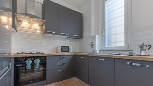 Eine moderne Küche mit grauen Schränken, einem eingebauten Backofen, einer Mikrowelle und einem Fenster mit Jalousien.