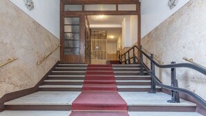 Eine Treppe mit Marmorwänden, einem roten Teppich und einer Holztür am oberen Ende.