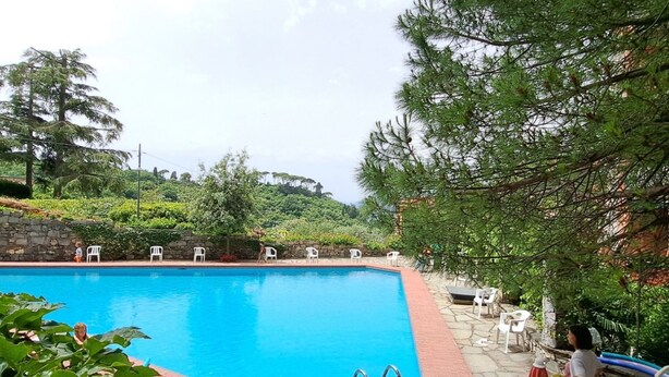 Une piscine bordée de pierres, entourée de verdure et agrémentée de quelques chaises blanches.