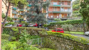 Un immeuble résidentiel à plusieurs étages, doté de balcons, d’un mur en pierre et de voitures garées.