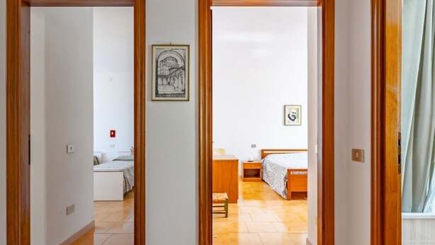 Un couloir mène à une chambre qui contient un lit, une table de chevet, une chaise et un tableau encadré accroché au mur.