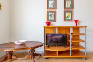 A wooden table with a bowl, a TV on a wooden stand, and framed artwork on the wall.