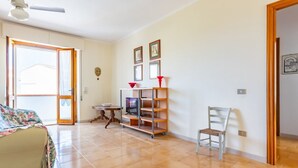 Une pièce comprenant un lit, un téléviseur posé sur un meuble, une chaise et une étagère avec des photos.